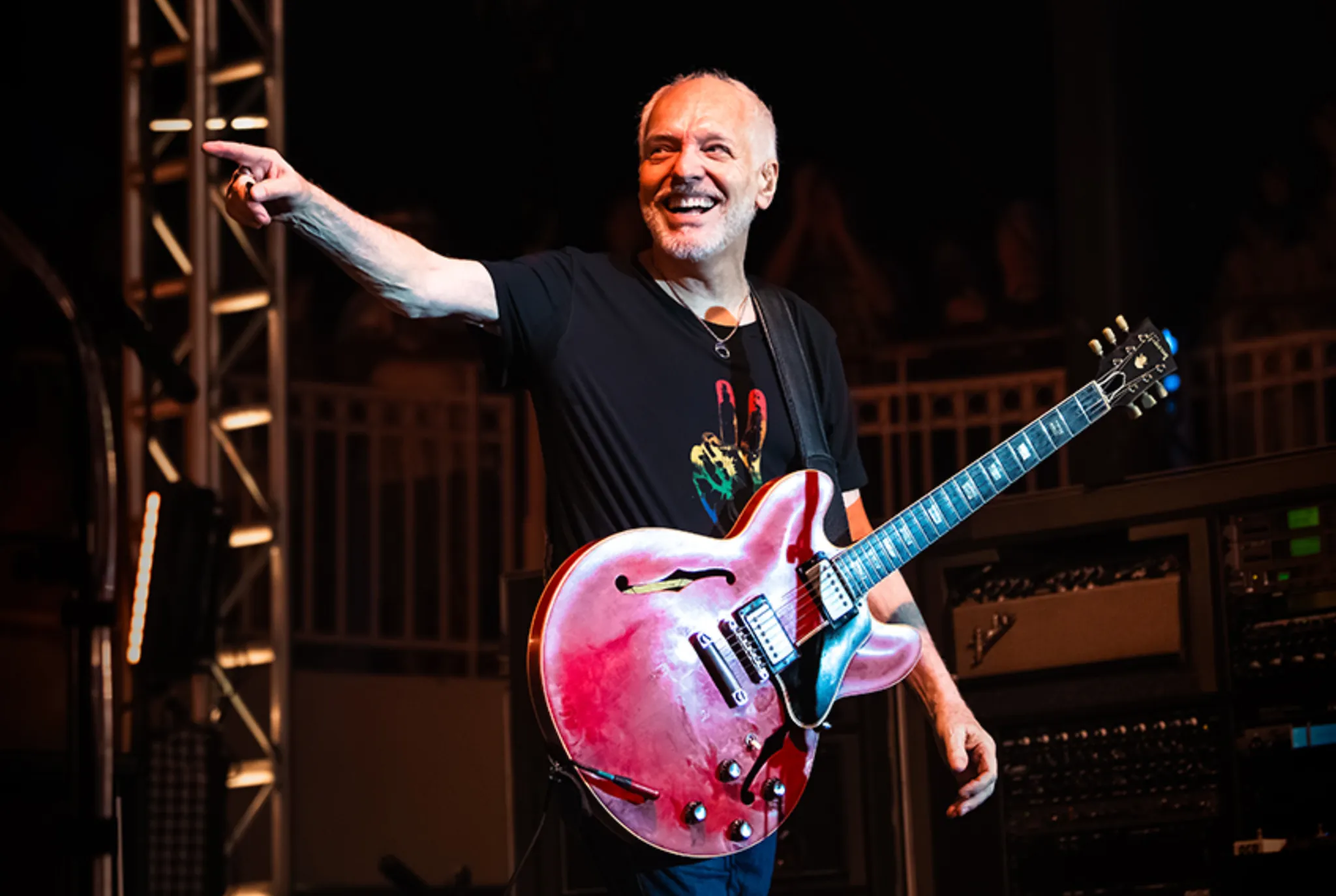 Peter Frampton smiling onstage with a red semi-hollow electric guitar